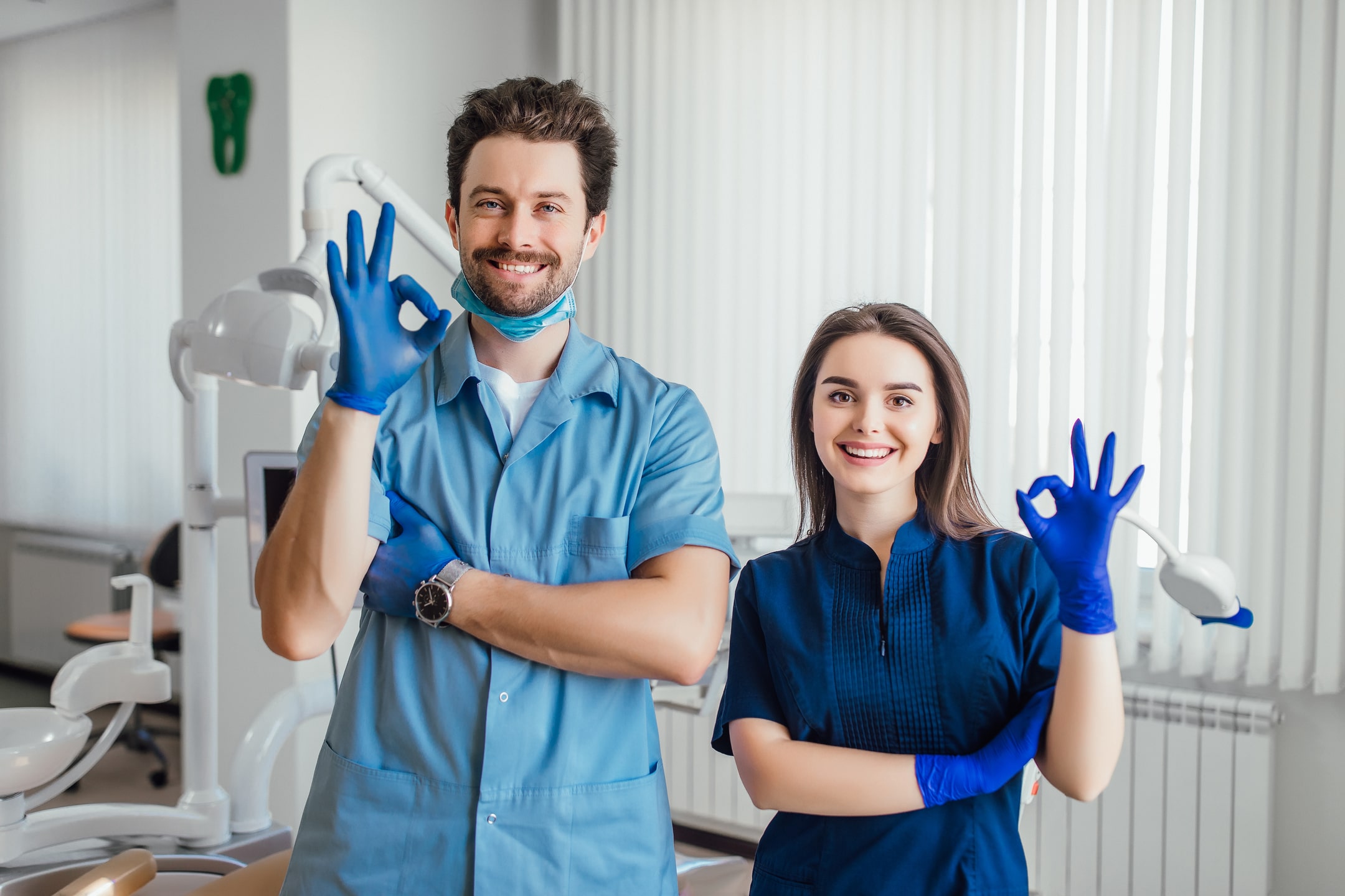 photo-smiling-dentist-standing-with-arms-crossed-with-her-colleague-showing-okay-sign-min